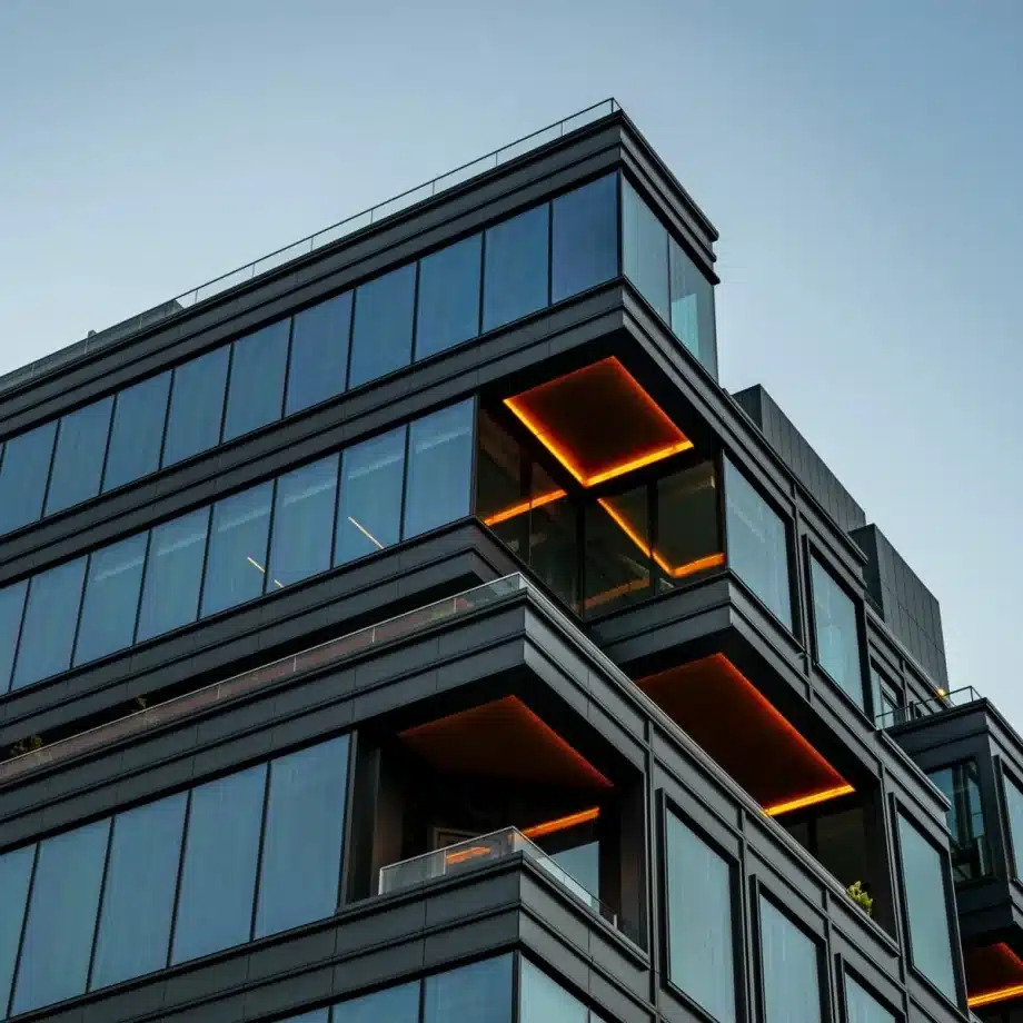 Modern glass building with orange-lit balconies.