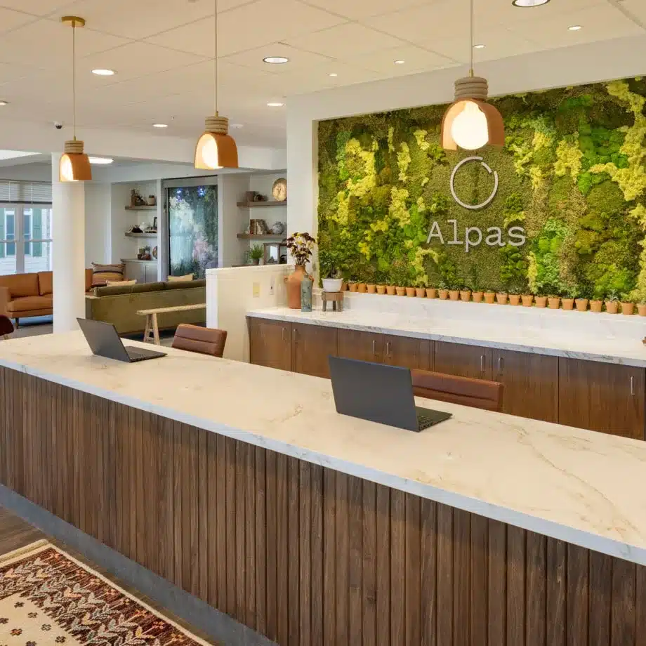 Reception area with moss wall art, laptops on wooden counter, and Alpas logo.