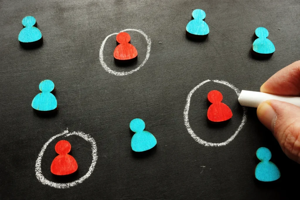 a hand drawing circles around small red wooden pieces representing the target audience -digitech