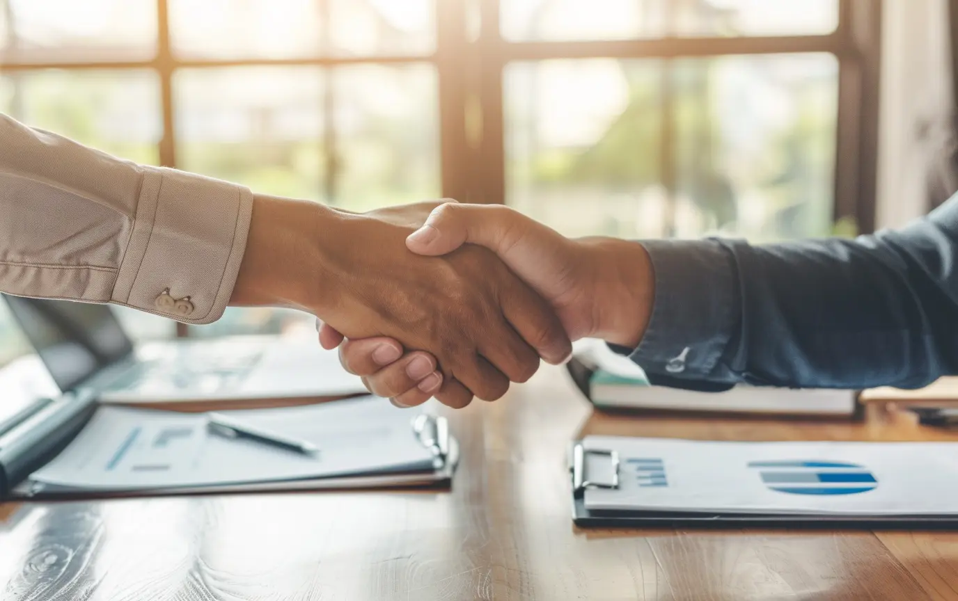 two hands shaking with charts and documents on a table- Digitech Austin